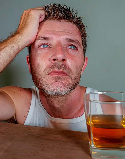 грустный мужчина сидит за столом со стаканом алкоголя